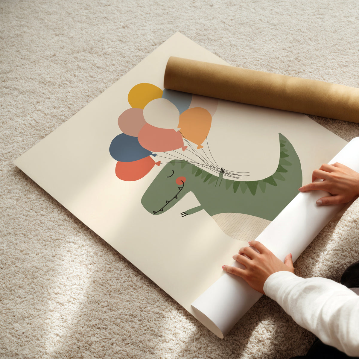 A large wall mural or poster featuring a green dinosaur holding colorful balloons, partially unrolled on a beige carpet with a person's hands visible rolling up the bottom edge. A brown cardboard mailing tube lies nearby.