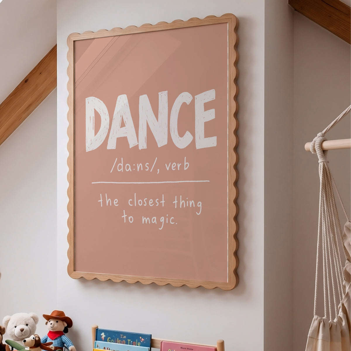 A framed typographic wall art print hanging on a light wall in a styled room. The print has a dusty pink background with the word “DANCE” in large white letters and a definition underneath, surrounded by a scalloped natural wood frame.