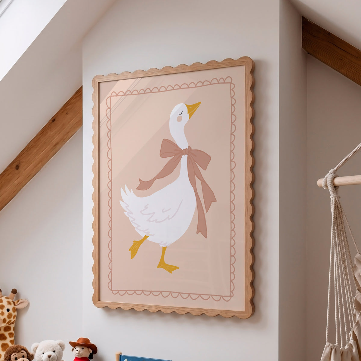 A framed wall art print featuring a white goose wearing a pink bow, hanging on a beige wall in a softly styled room with wood beams and small plush toys visible below.