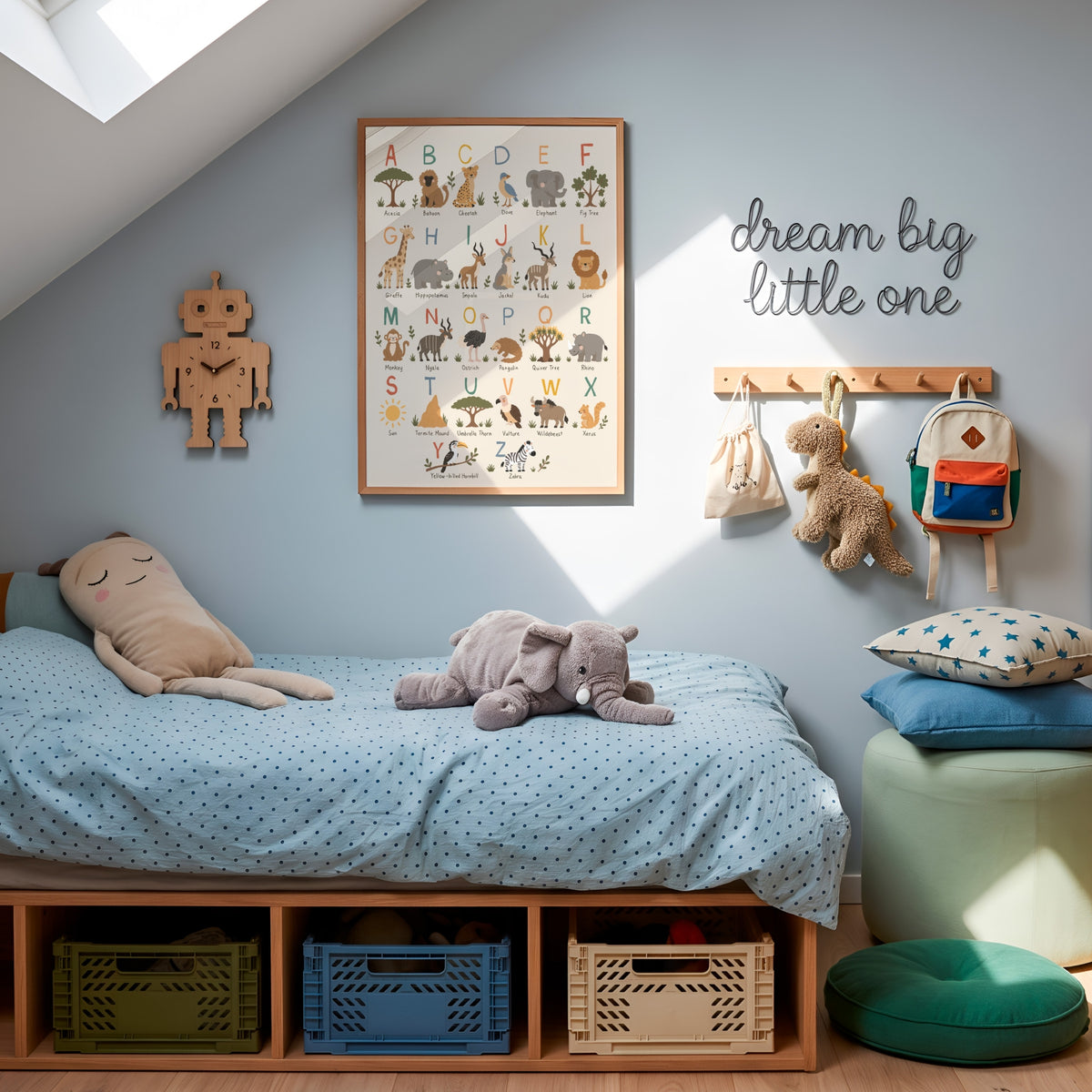 A styled children's bedroom corner with a low wooden bed frame, light blue bedding, plush toys, wall decor including an alphabet poster and 'dream big little one' sign, storage bins underneath the bed, and a mint ottoman with star pillows.