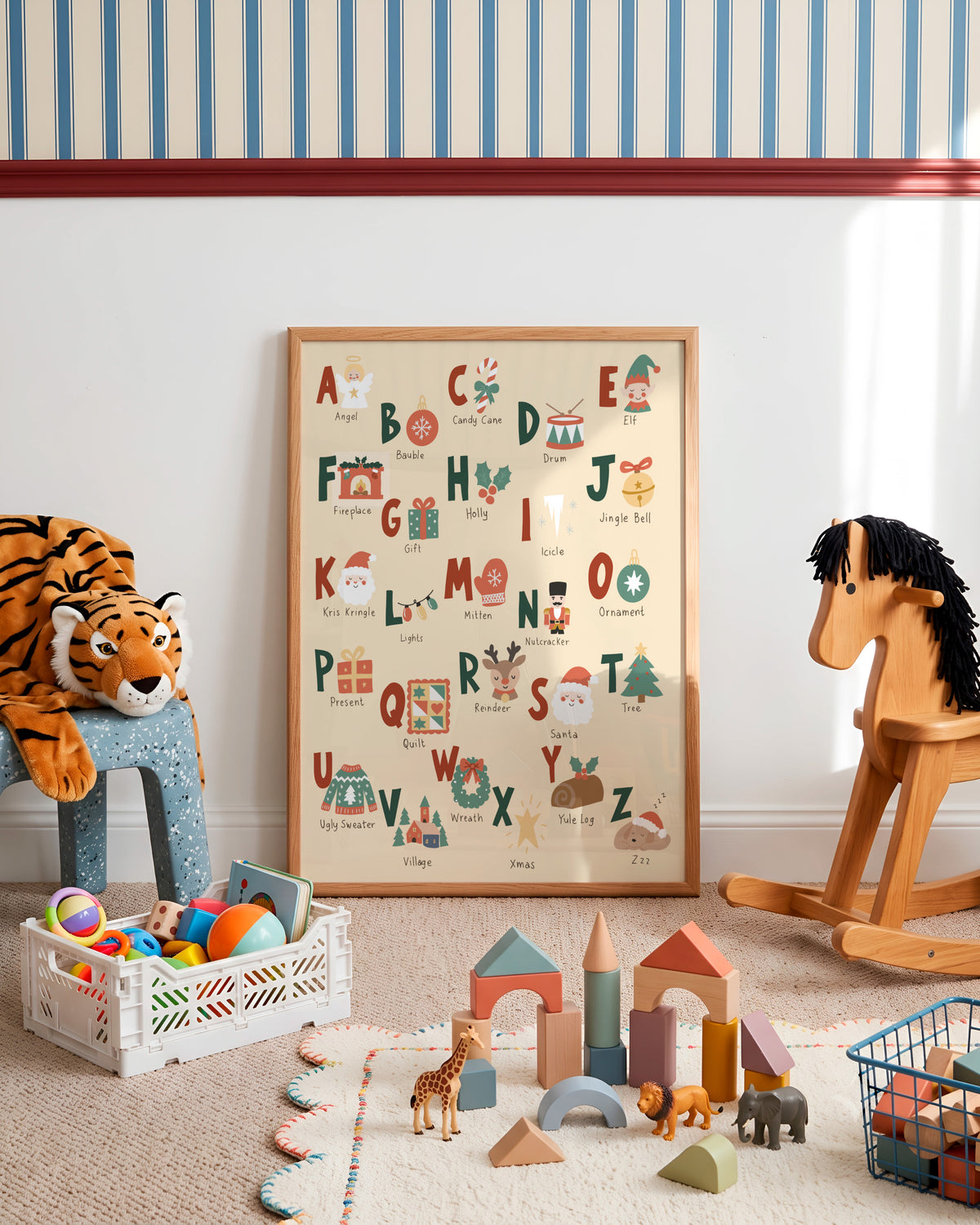 A framed alphabet nursery art print displayed on a wall in a styled children's playroom. The print features colorful illustrated letters and words with seasonal and everyday objects.