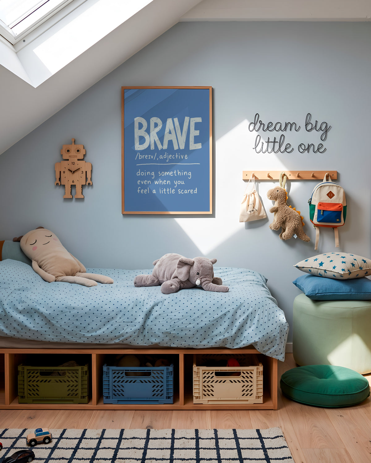 A styled children's bedroom corner with a low wooden bed, light blue bedding, stuffed toys, wall hooks, a framed 'BRAVE' poster, and a green pouf on a wood floor under a slanted roof.