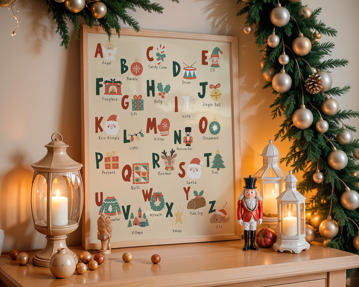 A framed Christmas alphabet art print displayed on a wooden mantel, surrounded by warm holiday decor including a lantern, nutcracker, pine garland with gold ornaments, and glowing candles.