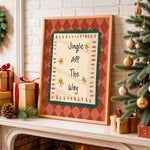 Framed Christmas wall art leaning on a fireplace mantel, surrounded by wrapped gifts, a green wreath, and a decorated Christmas tree. The print reads “Jingle All The Way” with gold stars and a red-and-cream patterned border.