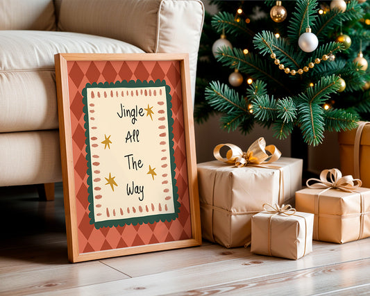 A framed Christmas art print leaning against a beige sofa on a wooden floor, next to wrapped gift boxes and a decorated Christmas tree. The print features the text 'Jingle All The Way' with gold stars on a cream background, bordered by a green scalloped frame and an orange argyle patterned border.