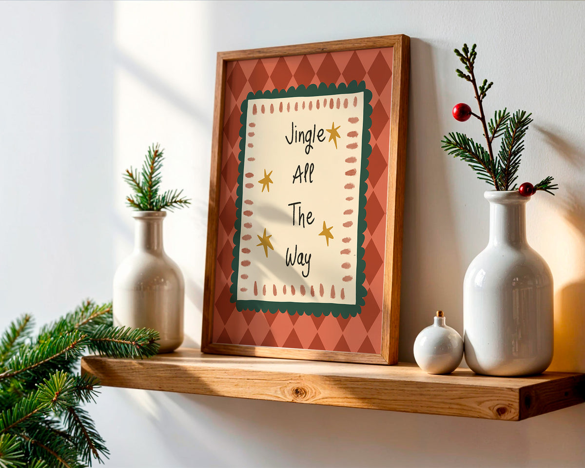 Framed wall art with the phrase 'Jingle All The Way' in a rustic wood frame, styled on a wooden shelf with white ceramic vases, evergreen branches, and small ornaments against a white wall.