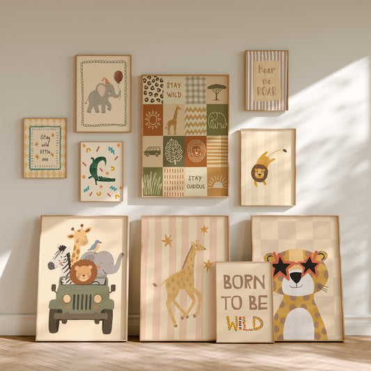 A set of framed children's wall art prints arranged on a wall and floor in a styled nursery setting. The prints feature safari-themed illustrations including an elephant, lion, giraffe, cheetah, zebra, sun, trees, and text phrases like 'Stay and see,' 'Stay curious,' 'Peace and love,' and 'BORN TO BE WILD.