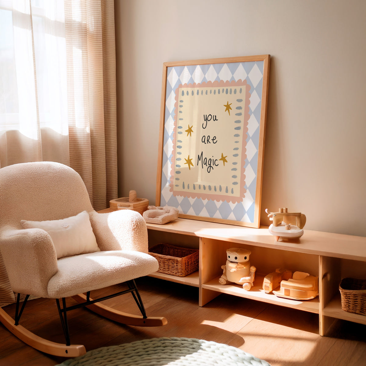 A framed nursery art print leaning on a wooden shelf in a softly lit nursery. The print reads 'you are Magic' in black script with small yellow stars, surrounded by a pale blue and white diamond pattern and a light wood frame.
