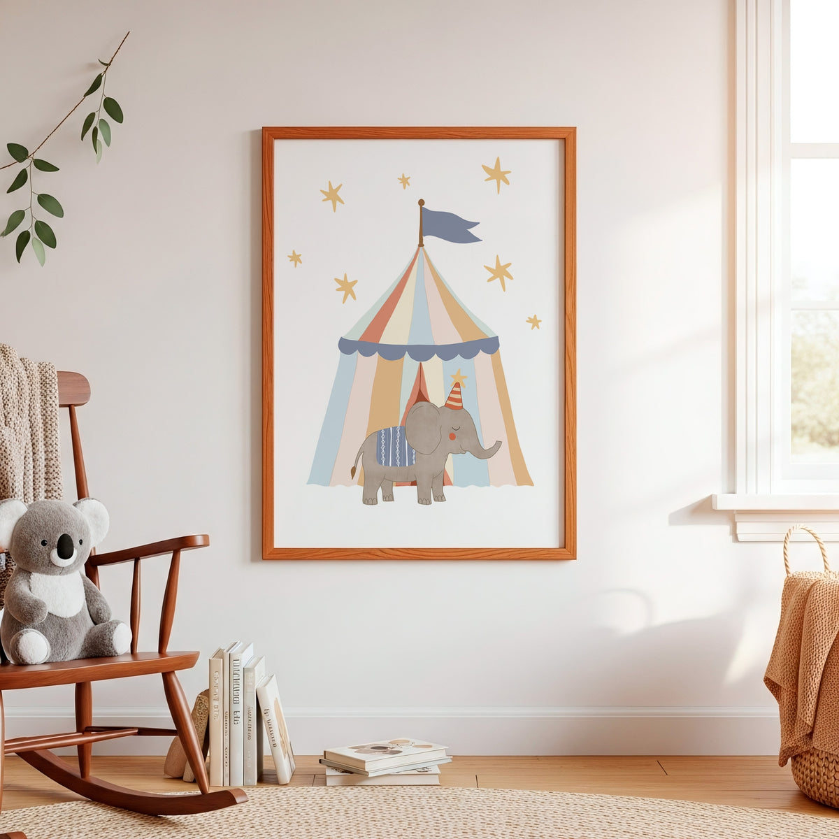 A framed nursery art print featuring a cartoon elephant under a striped circus tent, hung on a white wall in a softly styled child's room with a rocking chair, books, and a window.