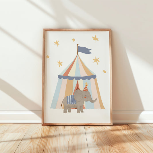 A framed children's art print leaning against a white wall on a light wood floor. The print shows a gray elephant wearing a party hat under a pastel striped circus tent with gold stars.