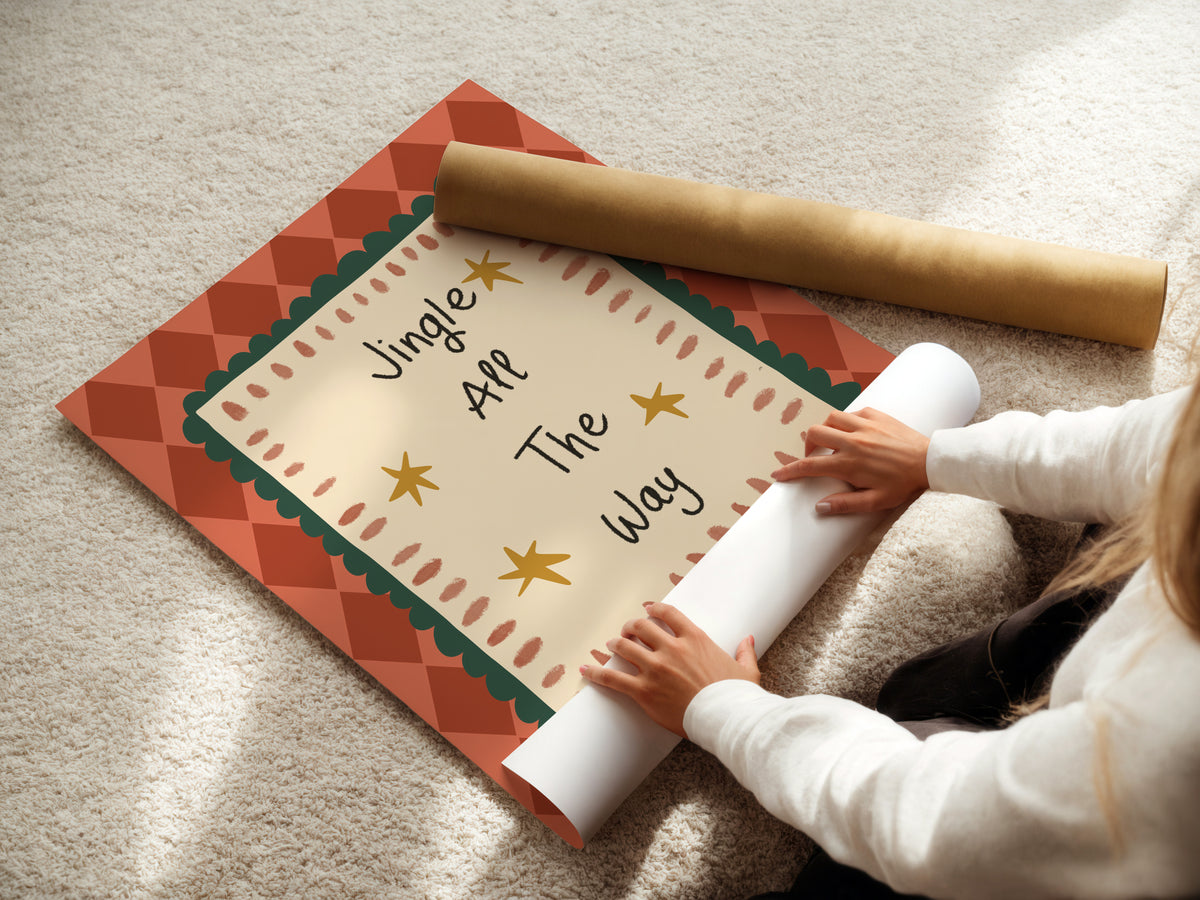 A person unrolls a decorative holiday poster on a beige carpet, with the printed message 'Jingle All The Way' visible and a rolled gold paper tube beside it.