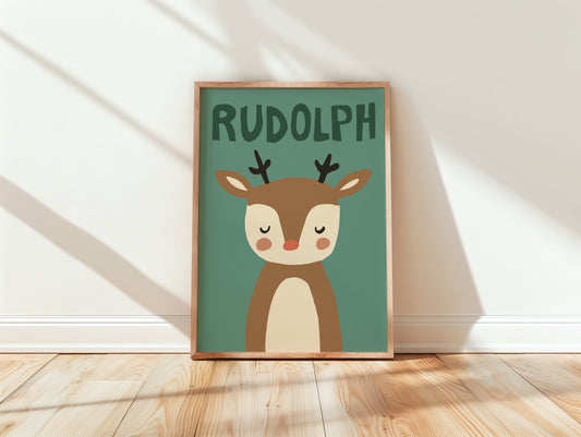 A framed art print featuring a cute cartoon reindeer named Rudolph on a muted teal background, leaning against a white wall on a light wood floor with soft window shadows.