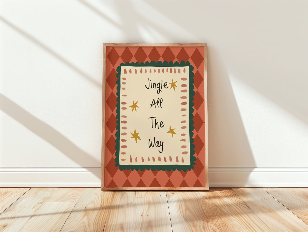 A framed holiday art print leaning against a white wall on a light wood floor. The print features the text 'Jingle All The Way' in a playful handwritten font, surrounded by a cream center panel with a dark green scalloped border, yellow stars, and a terracotta orange diamond-patterned frame.